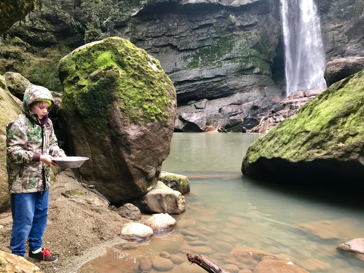 boy panning for gold beside waterfall on West Coast