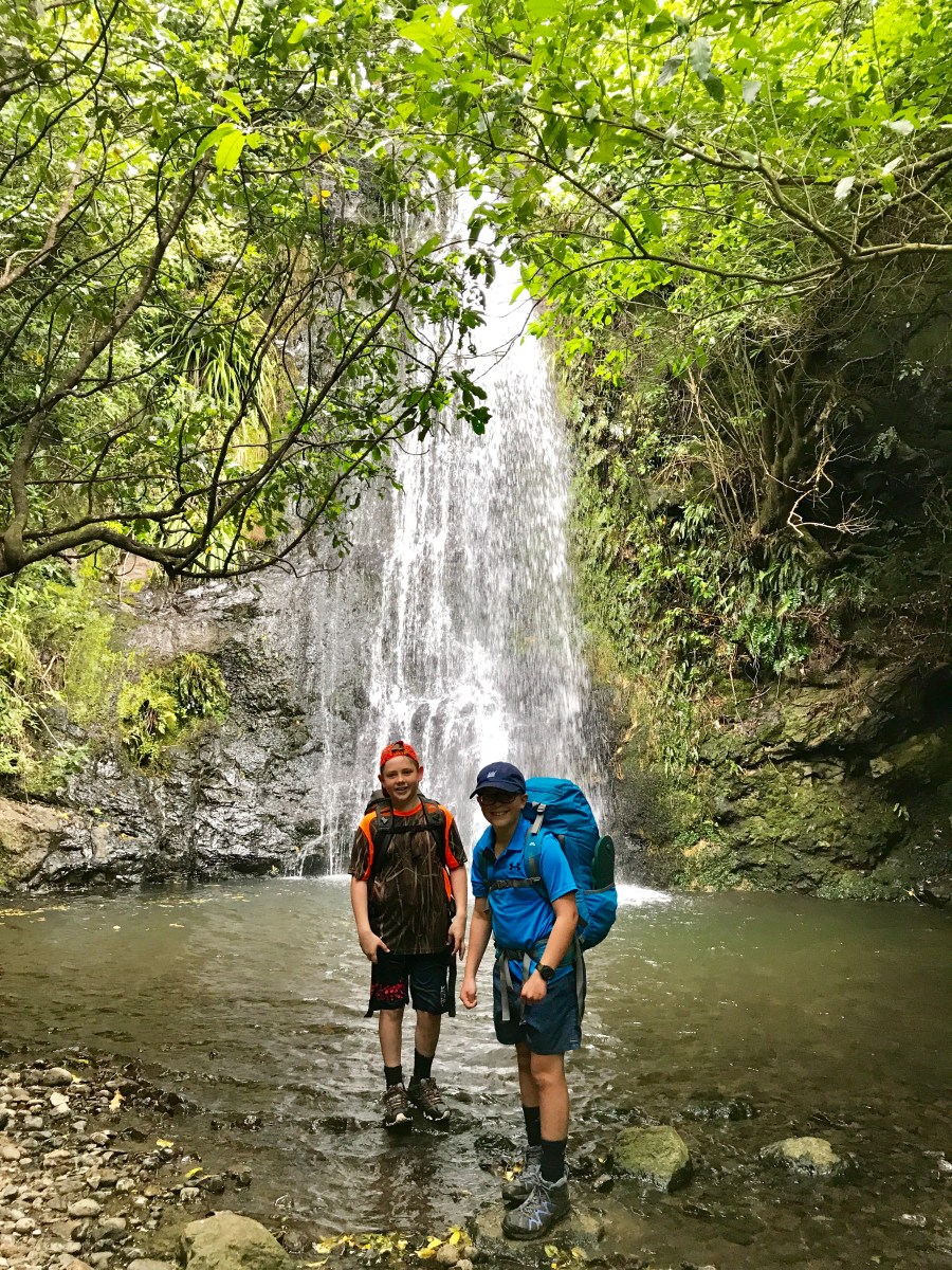 Two kids hiking and standing by a water fall